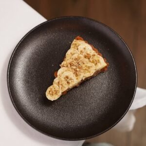 Tantalizing slice of banana cake served on a sleek black plate, perfect for dessert lovers.