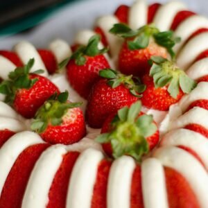 Close-up of a red and white striped bundt cake topped with fresh strawberries, perfect for sweet indulgence.