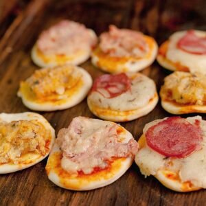 Tasty assortment of mini pizzas with cheese and toppings on a rustic wooden table, perfect for snacks.
