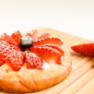 A delectable strawberry tart with a glossy finish on a wooden board, perfect for dessert lovers.