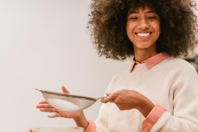 Happy woman with an afro sifting flour in a cozy kitchen setting, enjoying baking.